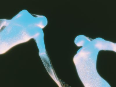 Two glowing pale blue translucent forms reaching toward each other across a black void, flecked with gold particles