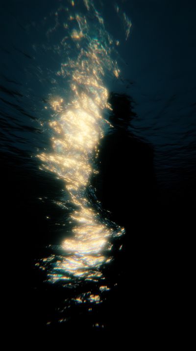 A diagonal cascade of golden light particles flows from upper left past a dark figure positioned to the right, the silhouette appearing to turn away or dissolve into the surrounding darkness.