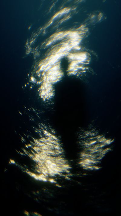 Swirling golden light forms turbulent circular patterns around a smaller centered figure, scattered points of luminescence creating a chaotic, enveloping effect like disturbed water.