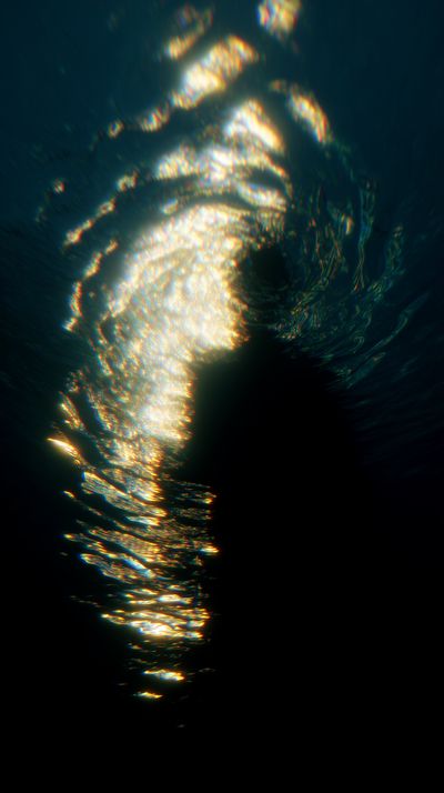 Concentric ripple patterns of golden light flow horizontally above a figure positioned lower right, with clear circular wave formations in the upper portion against deep blue-black.