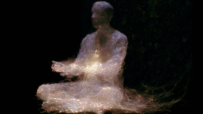 The same seated figure spun from fine warm filaments — gold and pale-white threads woven into a translucent body against pure black, a soft golden light glowing at its centre, faint faces dissolving in the dark behind.