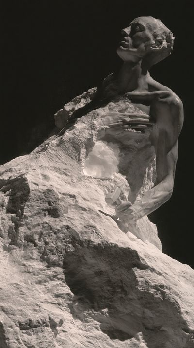 A gaunt figure rises from a massive block of uncut marble, face tipped to the light, a mallet still in one hand.