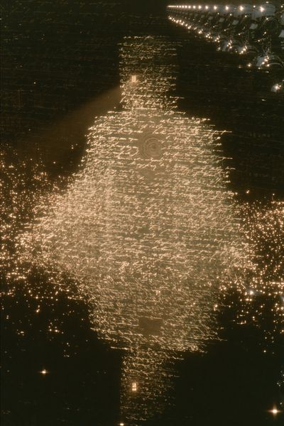 A dense glowing cocoon woven from amber text hangs in darkness, chrome androids observing from a balcony above.