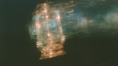 An amber and blue lantern blurs into horizontal light trails beside a faint rectangular window in darkness.