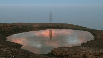 A faint ghostly figure stands in blue fog beyond a rocky tide pool that reflects it, with pink clouds and swirling water.